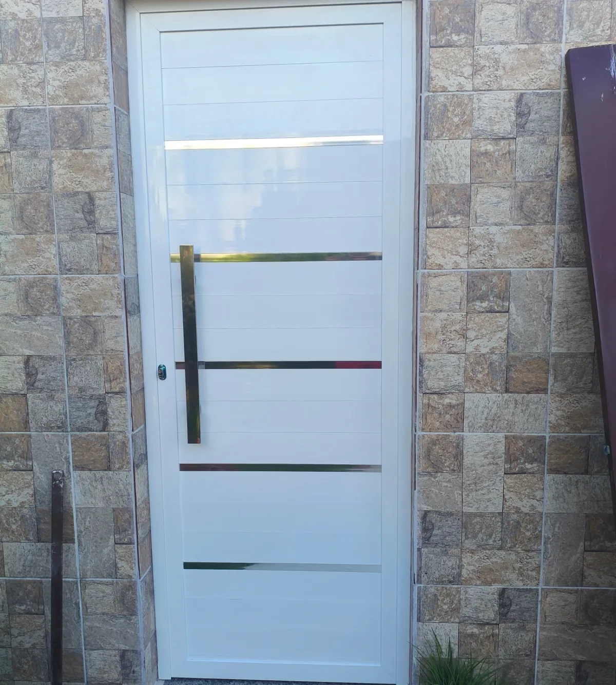Porta de alumínio branco com frisos metálicos instalada em parede revestida
